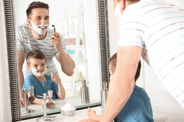 Dad shaving and little son imitating him in bathroom - Фото, зображення