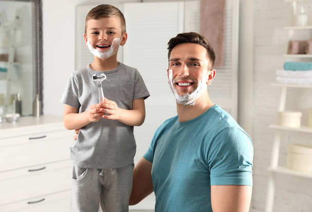 Dad and his little son with shaving foam on faces in bathroom - Photo, image