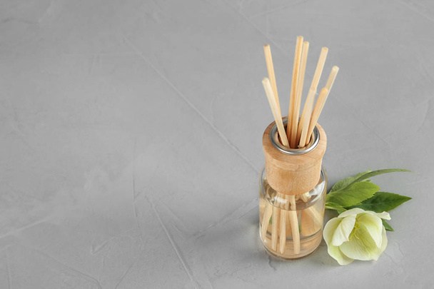 Aromatic reed freshener and flower on grey table, space for text - Foto, imagen