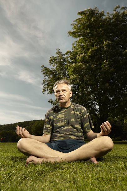 Пожилой человек, практикующий медитационные ритуалы в летнем городском парке
 - Фото, изображение