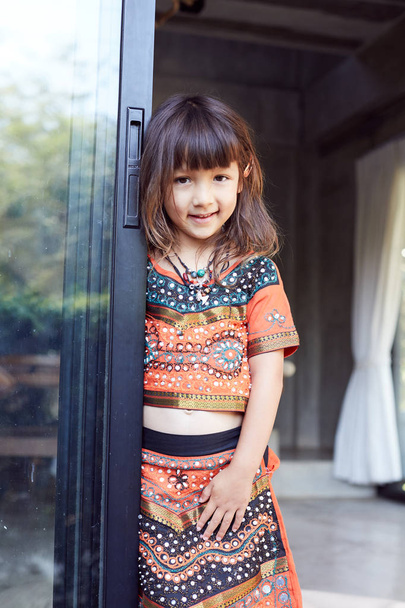  Autentyczne portret Pretty Thai baby girl pozowanie na zewnątrz, ubrany w tradycyjny kolorowy strój, biżuteria, będąc w dobrym nastroju, uśmiechając się i patrząc na kamerę. Atrakcyjne dziecko ciesząc się życiem - Zdjęcie, obraz