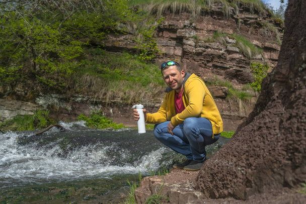 山の川の近くで白いサーモスからコーヒーを飲む男 - 写真・画像