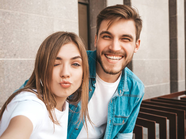 Smiling beautiful girl and her handsome boyfriend in casual summer clothes. Happy family taking selfie self portrait of themselves on smartphone camera. Having fun on the street background  - Foto, Bild