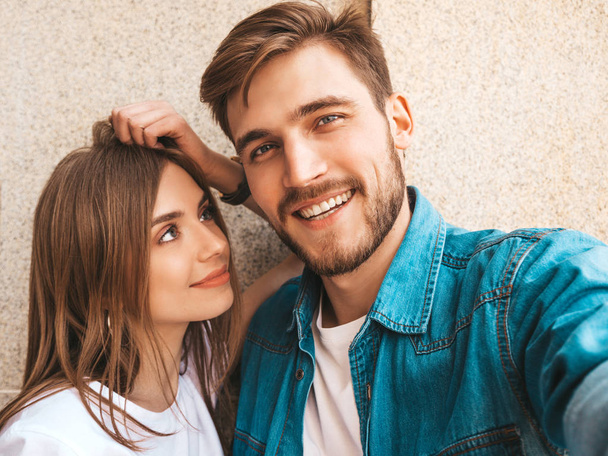 Smiling beautiful girl and her handsome boyfriend in casual summer clothes. Happy family taking selfie self portrait of themselves on smartphone camera. Having fun on the street background  - Fotografie, Obrázek