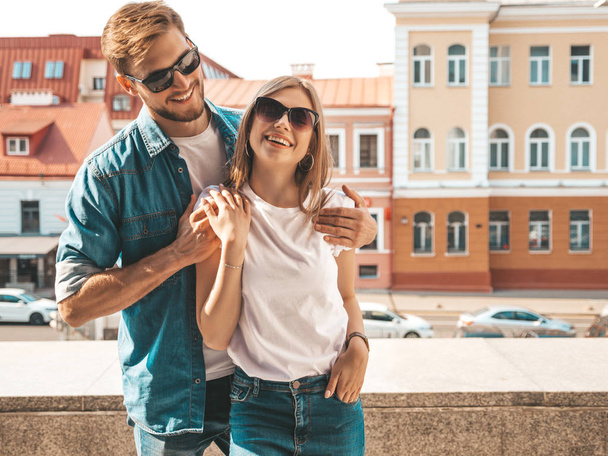 Smiling beautiful girl and her handsome boyfriend. Woman in casual summer jeans clothes. Happy cheerful family. Female having fun on the street background in sunglasses.Looking at each other - 写真・画像