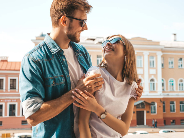 Smiling beautiful girl and her handsome boyfriend. Woman in casual summer jeans clothes. Happy cheerful family. Female having fun on the street background in sunglasses.Looking at each other - Foto, immagini