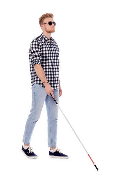 Young blind person with long cane walking on white background - Foto, imagen