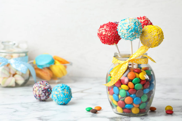 Yummy bright cake pops in glass jar full of candies on table. Space for text - Valokuva, kuva