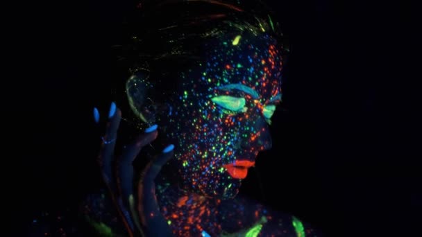 Femme mannequin en néons posant en studio, portrait de belle fille,. visage peint avec éclat dans la peinture sombre
. - Séquence, vidéo