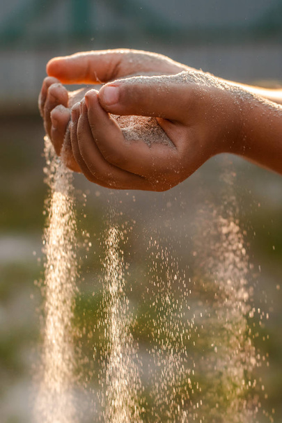 Children's hands release the falling sand. Sand flowing through your hands in the sunset sunlight. - Φωτογραφία, εικόνα