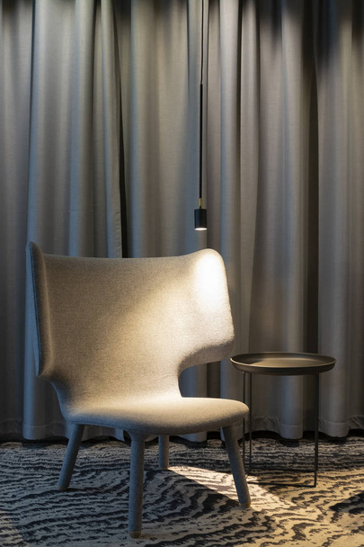 Modern interior with an empty comfortable armchair with light and table near curtains. Left to right direction - Фото, изображение