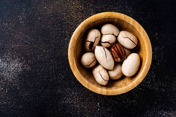 Organic dried pecan in wooden bowl on dark slate background. Top view with copy space.  - Foto, afbeelding