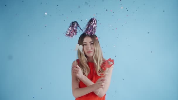 Beautiful girl in party hat are dancing under falling confetti and Balloons on a blue background. - Felvétel, videó