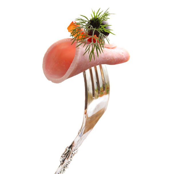 A delicious piece of ham with olive, tomato and dill pinned on a fork. - Fotó, kép