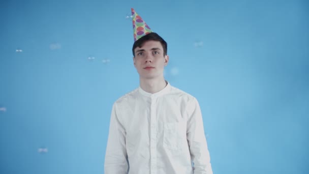 Young man in party hat are standing under soap bubble on a blue background. - Footage, Video