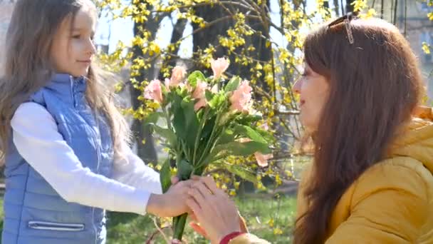 Happy mothers day. Child daughter congratulates mom and gives her a flowers. Mum and girl smiling and hugging. Family holiday and togetherness. - Video