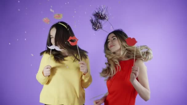 Piękne dziewczyny w zabawnych kapelusze tańczą pod konfetti na fioletowym tle. - Materiał filmowy, wideo