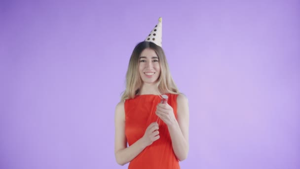 Young woman exploding confetti cracker on a purple background. - Filmagem, Vídeo