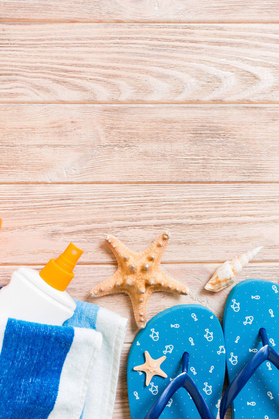 Top view of Beach flat lay accessories. sunscreen bottle with seashells, starfish, towel and flip-flop on wooden board background with copy space - Photo, Image