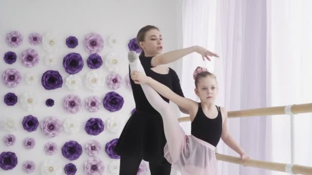 Преподаватель балета, профессиональная балерина, обучает девочек движениям ног и наклоняется в балетном баре во время индивидуального урока в танцевальной школе
. - Кадры, видео