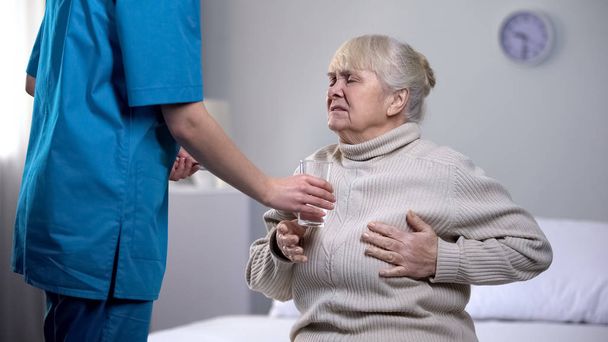 Νοσοκόμα δίνοντας παυσίπονα ηλικιωμένη κυρία που πάσχουν από καρδιακή προσβολή, θεραπεία - Φωτογραφία, εικόνα