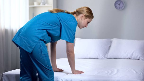 Young nurse preparing clean bed-linen in rehabilitation center, good service - Photo, image