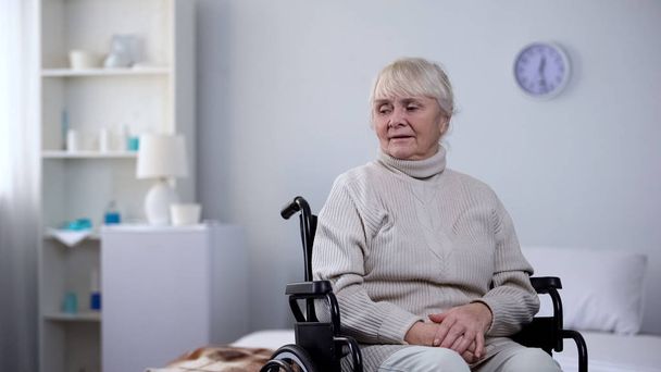 Upset senior woman in wheelchair sitting alone in rehabilitation center room - Фото, зображення