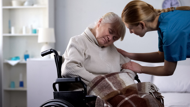 Genç gönüllü, yaşlı kadını uyandırıyor tekerlekli sandalyede uyuyor, hastane bakımında. - Fotoğraf, Görsel