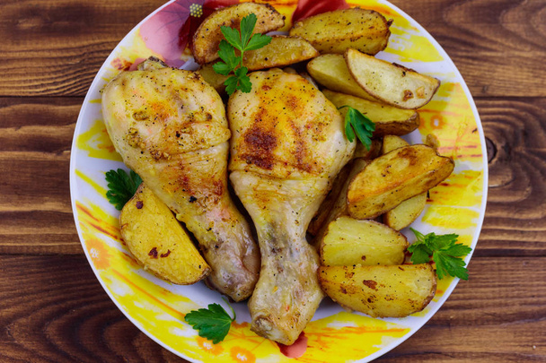 Bacchette di pollo al forno con patate in un piatto sul tavolo di legno
 - Foto, immagini