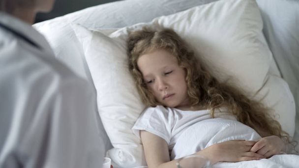 Sick weak girl lying in bed in hospital, doctor examining patient, healthcare - Photo, image