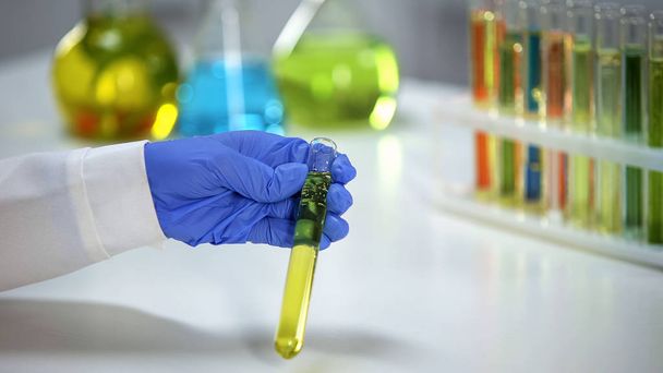 Lab assistant holding tube with yellow transparent liquid, extract for perfumery - Фото, изображение