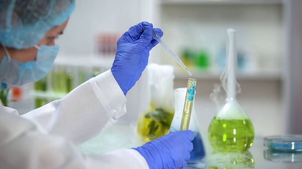 Scientifique ajoutant un liquide bleu dans un tube avec une substance huileuse jaune, essai de biocarburant
 - Photo, image