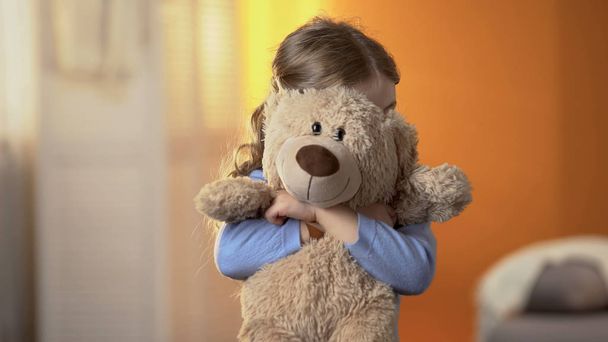 Preschool shy girl hiding behind teddy bear, childish psychological problems - Fotó, kép