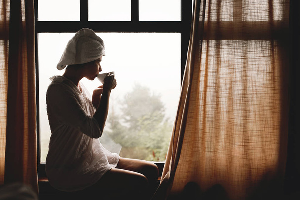 Красива щаслива молода жінка п'є каву або чай, сидячи в б
 - Фото, зображення