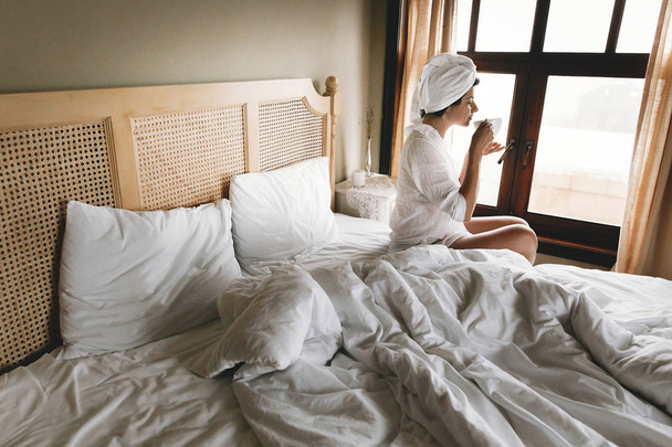 Bella felice giovane donna che beve caffè a letto in camera d'albergo
 - Foto, immagini