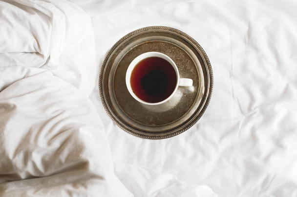 Chá na xícara branca na bandeja vintage de metal na cama branca, vista superior. E
 - Foto, Imagem