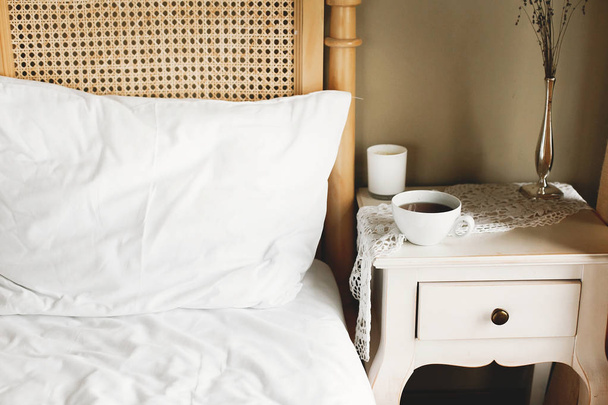 Cama com lençóis brancos e mesa de cabeceira vintage com copo branco de c
 - Foto, Imagem