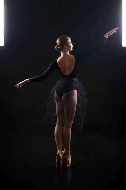 Charming girl ballerina in a black suit, is dancing a ballet in the light of the contour . - Foto, afbeelding
