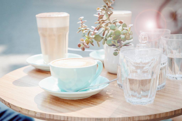 Φλιτζάνι καφέ καπουτσίνο και γυαλί με καφέ λάτε σε ένα καφέ του δρόμου. Αποτέλεσμα ηλιοθαμβωτικής ισχύος. Παστέλ τονισμένη φωτογραφία - Φωτογραφία, εικόνα