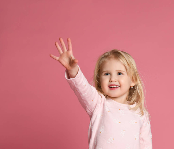 Little cute girl child blonde in a pink suit is shy on a pink background - Фото, изображение