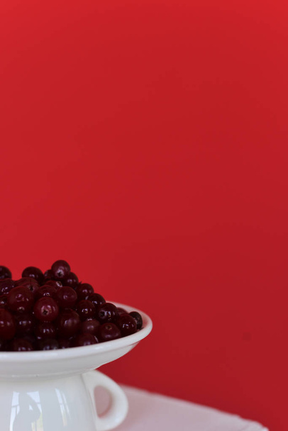 Kırmızı bir arka plan üzerinde kırmızı frenk üzümü berry ile beyaz bir fincan. Une tasse blanche avec des baies de cassis sur un fond rouge - Fotoğraf, Görsel