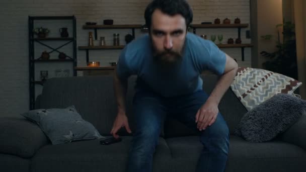 Young man sitting on the sofa, taking remote control tv and turn on TV. - Video, Çekim