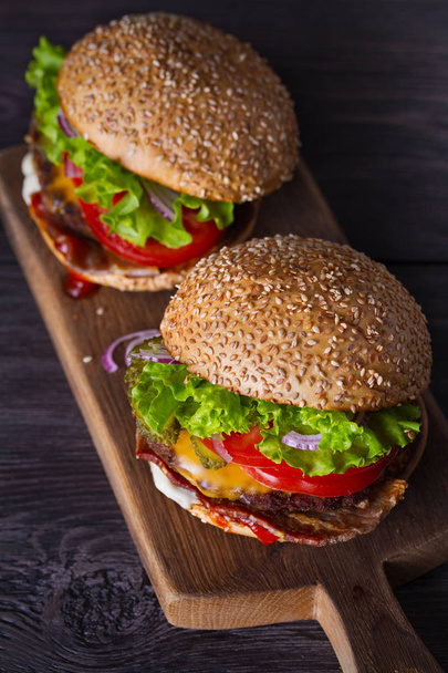 Delicious homemade beef burgers with bacon on wooden chopping board. vertical - Fotoğraf, Görsel