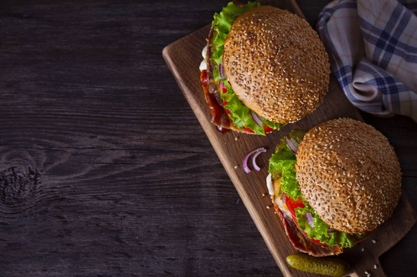 Delicious homemade beef burgers with bacon on wooden chopping board. overhead, horizontal, copy space, food background - Foto, Imagem