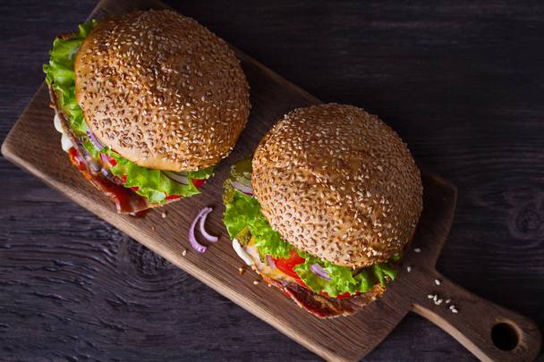 Delicious homemade beef burgers with bacon on wooden chopping board. overhead, horizontal - Foto, Imagem