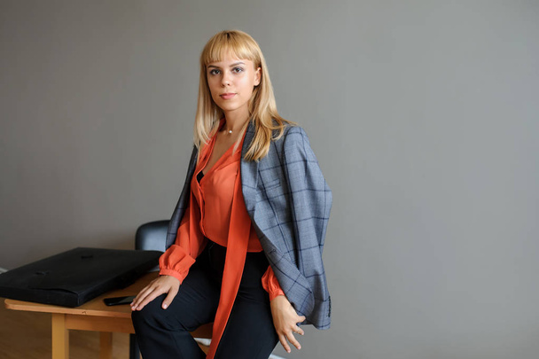 A business woman on the office desk in a grey jacket, grey background - Foto, imagen