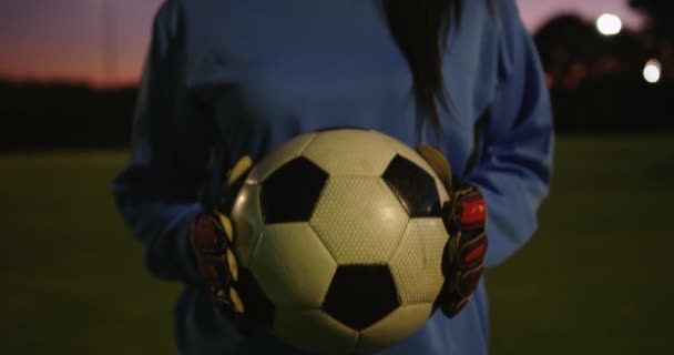 Portrait of happy Caucasian female soccer player smiling while holding ball on soccer field at night. 4k - 映像、動画