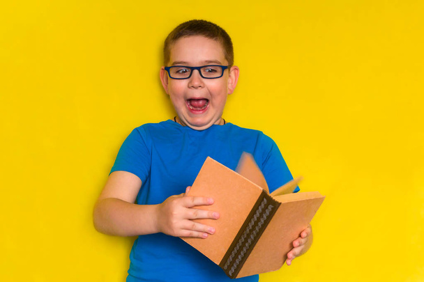 funny little boy with glasses and blue t-shirt holding a book and screaming with fear, lazy student and back to school concept - Fotografie, Obrázek