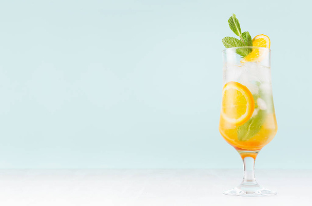 Fresh orange cocktail with slices fruits, mint, straw, ice cubes in misted glass on white wood table and blue color wall, copy space. - Photo, image