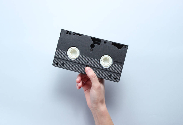 Hand houdt video cassette op grijze achtergrond. Retro stijl, popcultuur, minimalisme, bovenaanzicht - Foto, afbeelding